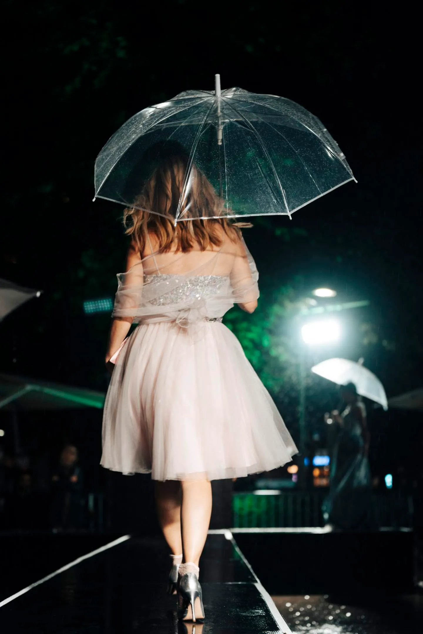 Dame mit schwarzem Kleid mit offenem Regenschirm in der Hand, läuft von der Kamera weg